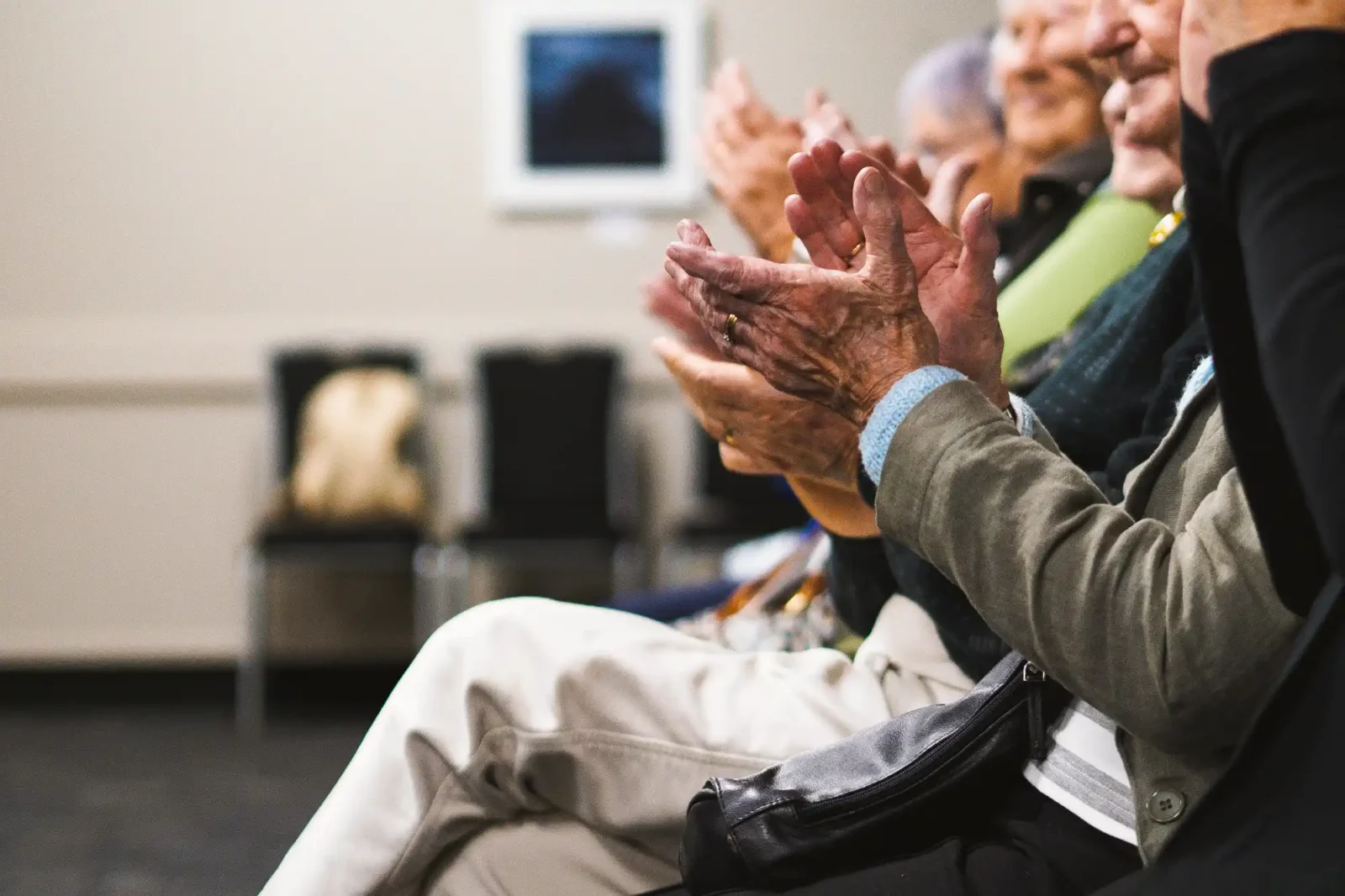 A group of elderly people sitting in a row and clapping their hands.