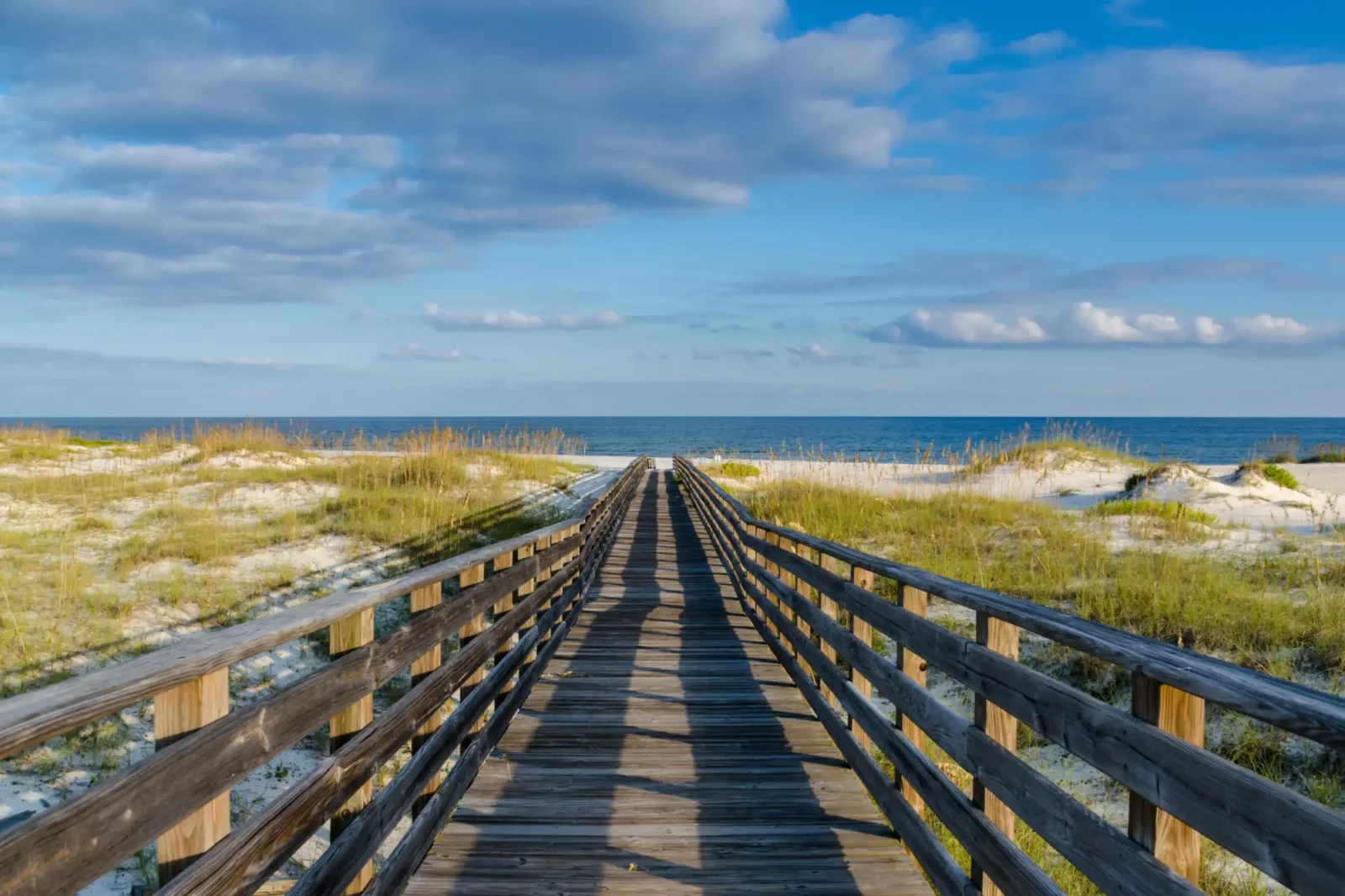 An old wooden boardwalk going out to a gulf shore beach.