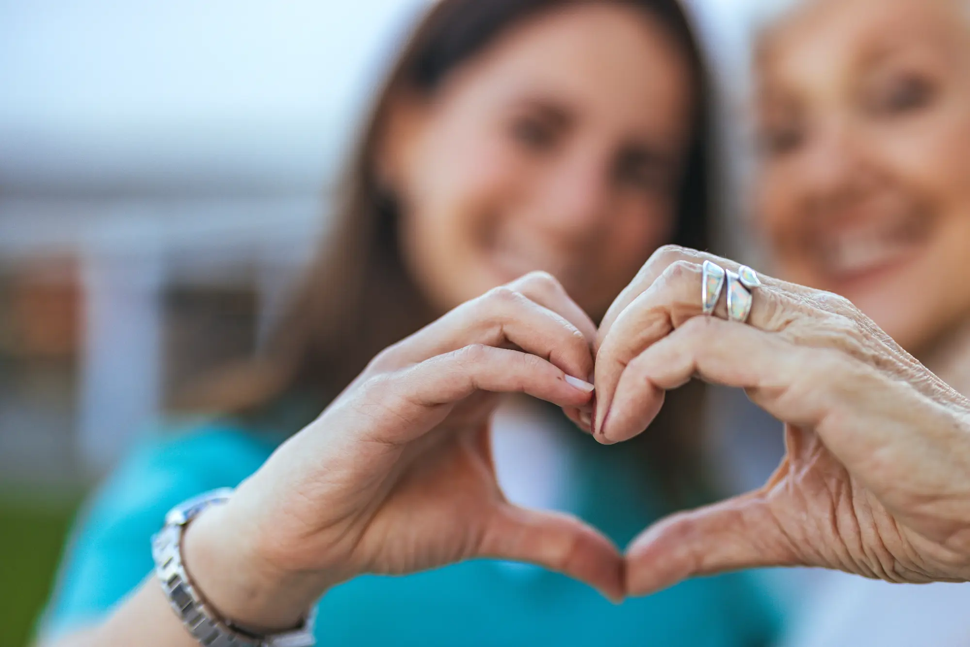 A younger woman and older woman's hands together in a heart shape.
