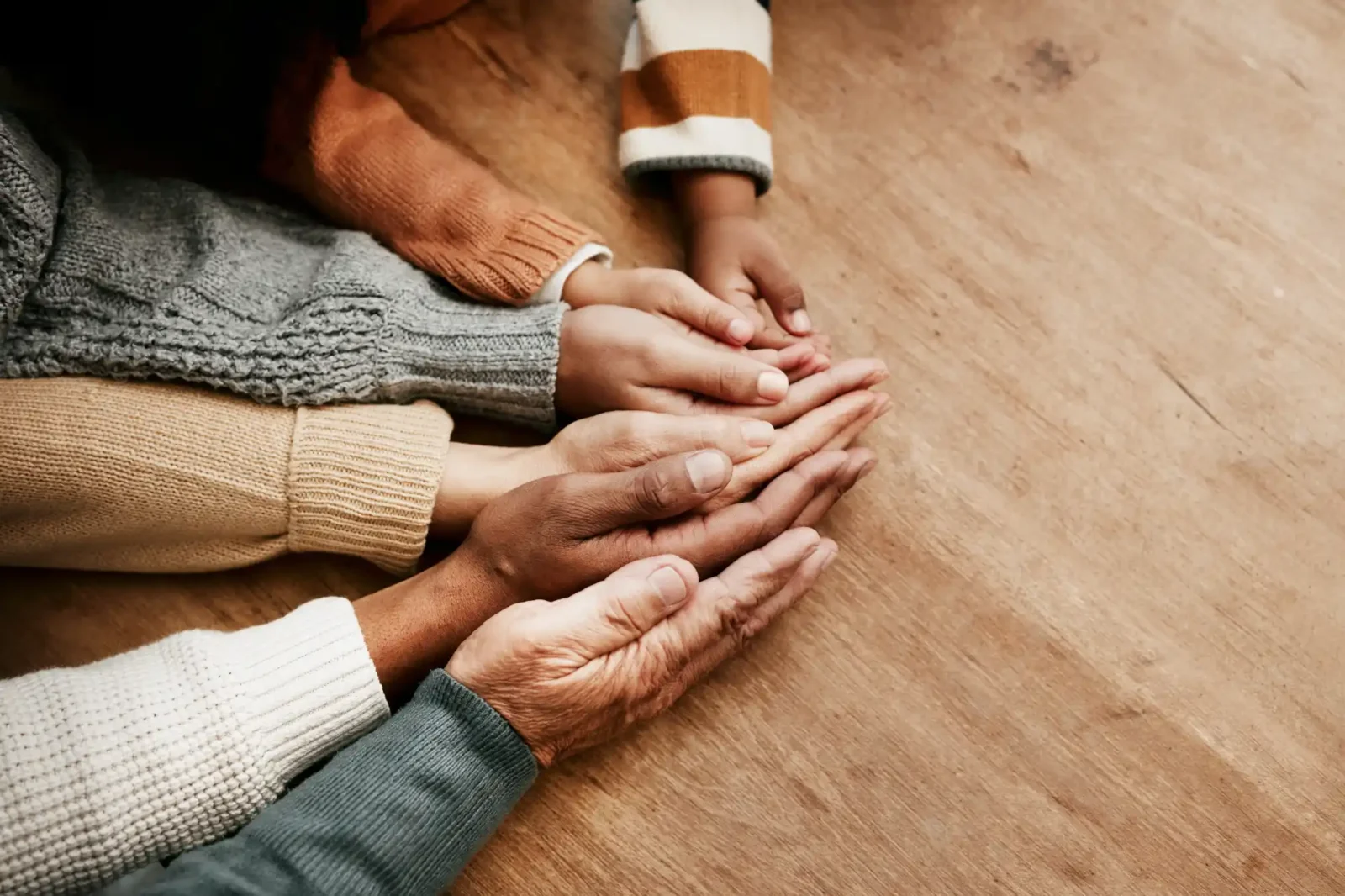 A group of six hands cupped together starting with a little kid's hand all the way to an elderly wrinkled hand.