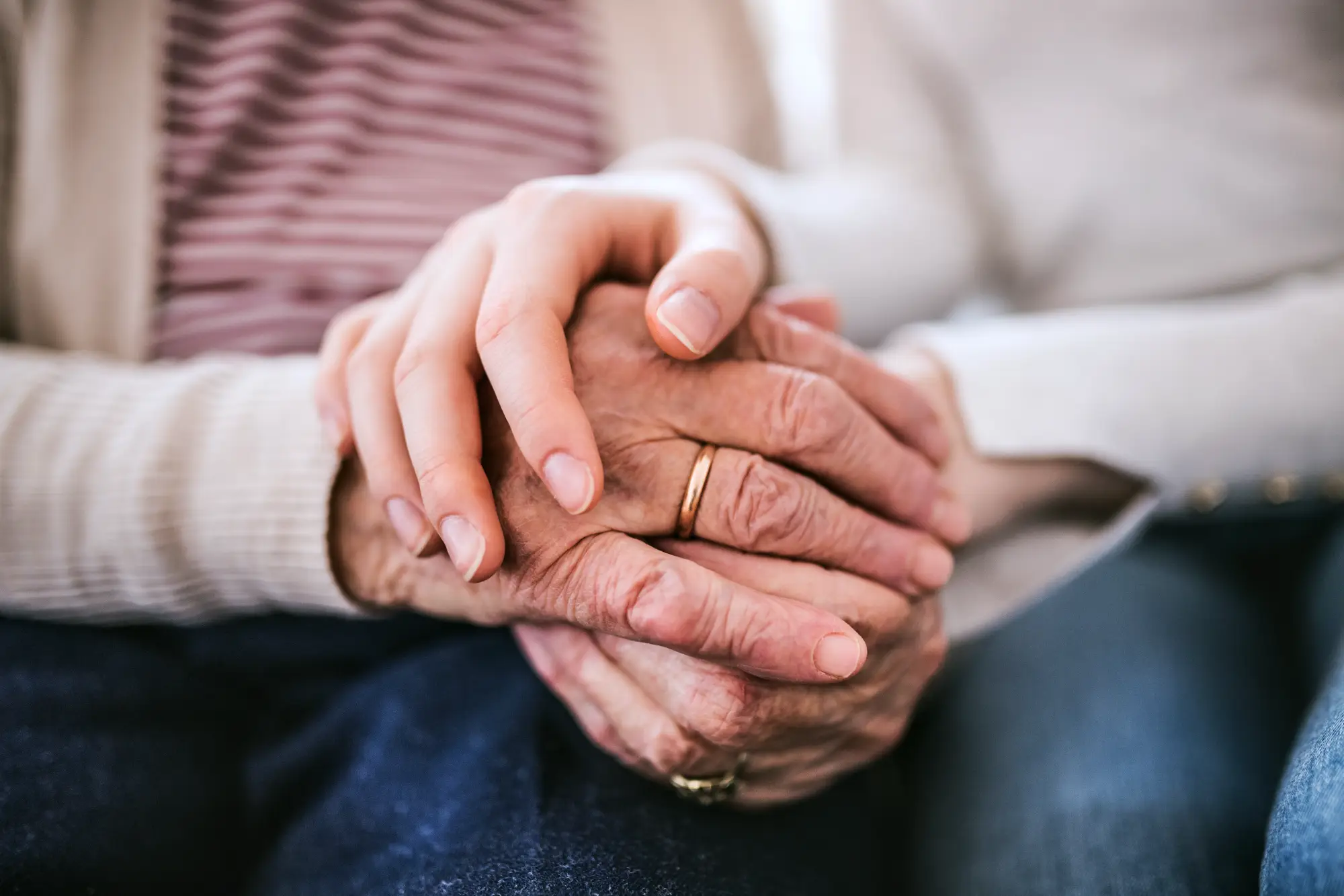 A young persons hands cupping an elderly persons hands.
